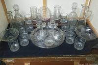 Full set of vintage glass barware including decanters, glasses, bowls, and trays placed on table with dark cloth