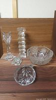 Five pieces of cut crystal tableware and decorative items arranged on a wooden surface: a tall vase, a large bowl with floral etching, a leaf-shaped dish, a rectangular block piece, and a small figurine. The crystal is clear with detailed floral engravings and cut designs.