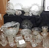 Display of all cut glass tableware including bowls, plates, and lidded containers on steps against black background.