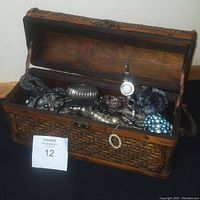 Wicker chest opened showing costume jewelry inside including pearl necklaces, bracelets, and brooches