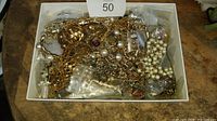 Lot of vintage and costume jewelry in a white box including chains, rings, faux pearl necklaces, and earrings mainly gold and silver tones.