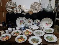 Wide view of assorted handpainted plates, small cups, jars, pitchers, and crystal decanters on display
