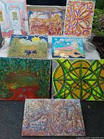 Eight original artworks by local artist displayed outdoors for inspection, showing various styles, subjects, and canvas sizes.