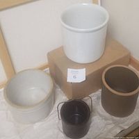 Four stoneware crocks of varying sizes shown together from a front angle on a cloth surface near a cardboard box.