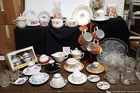 Overview of the lot showing all cups, saucers, glass bowls, mugs, and other ceramic items arranged on two levels with black cloth background.