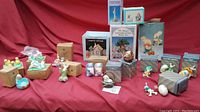 Wide shot of vintage Easter decor items spread on red cloth background showing various bunny and lamb figurines, boxed Avon items, and salt & pepper shakers.