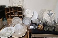 Wide view of the vintage glassware lot including plates, bowls, decanter, basket, and glass dishes in various styles and colors needing cleaning.