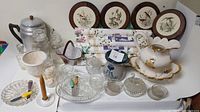 Overall lot display showing vintage kitchenware items, glass jars, ceramic pieces with floral motifs and gold trim, decorative plates with birds, and wallpaper rolls with coffee-themed prints.