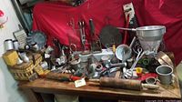 Photo showing a spread of vintage kitchen utensils including strainers, rolling pins, molds, and metal measuring cups on a table with a red backdrop.