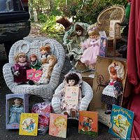 Photo showing white vintage wicker chairs with porcelain dolls seated and vintage storybooks arranged in front, plus brown wicker chairs in the background.