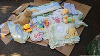 Overview of Winnie the Pooh themed nursery items spread on cardboard outdoors, showing bedding and stuffed animals