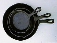 Three cast iron skillets stacked by size showing black seasoned surfaces and loop handles