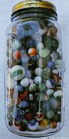 Full fruit jar filled with assorted glass marbles in various colors and patterns, photographed from above showing marbles densely packed inside.