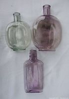 Set of three antique whiskey bottles including two amethyst pumpkinseed flasks and one clear pumpkinseed flask.