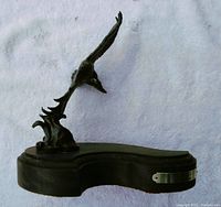 Side view of bronze eagle statue on curved wooden base showing profile and overall shape.