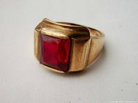 Three-quarter front view of yellow gold ring with square-cut red gemstone set in bezel shoulders.