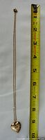 Full length of gold chain necklace with heart-shaped locket next to measuring tape showing length about 18 inches.