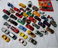 Photo showing over 40 diecast cars arranged on white surface including various small model cars with different colors and designs