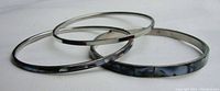Three silver-tone bracelets including two plain bands and one with mother of pearl inlay, photographed on white background.