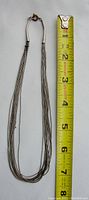 Full length view of the multi-stranded liquid silver necklace alongside a tape measure showing approximately 14 inches in length