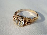 Gold ring with a large, round faceted clear crystal stone in detailed filigree setting shown from an angle.
