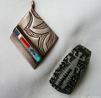 Photo of two Native American style jewelry items: diamond shaped silver pendant with multicolor inlay and etched designs, small brooch pin with black and silver geometric etched pattern.