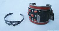 Photo of two Native American silver jewelry pieces: a wide cuff bracelet with coral inlay and coral nuggets, and a slender eagle motif watchband.