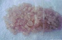 Close-up photo of loose polished and drilled rose quartz crystals inside a clear plastic bag on a textured white surface.