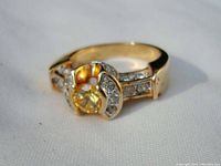 Close-up side angle of gold colored ring with yellowish central crystal and small crystals on sides and band.