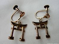 Close-up photo of a pair of Asian style clip-on earrings with torii gate design, screw-back mechanism visible.
