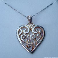Close-up front view of a sterling silver heart-shaped filigree pendant on a fine chain necklace, showing intricate open scrollwork design.