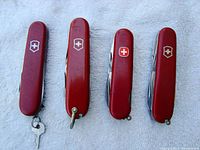 Four red Swiss Army pocket knives side by side showing Swiss cross logos on handles and attached keys/loops.