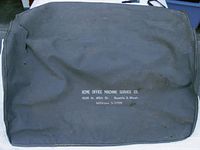 Original black fabric cover for the typewriter with ACME Office Machine Service Co. branding and address in Seattle, Washington.