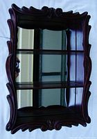 Front angle view of vintage wooden wall shelf showing mirror back, two shelves, and ornate carved wooden frame in dark walnut color.