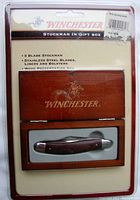 Photo shows Winchester 3 Blade Stockman pocket knife in original sealed plastic packaging with wooden gift box. The packaging artwork includes product details and brand markings.