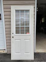 Front view of white exterior door with glass panel and grid pattern. Shows two lower recessed panels and glass panel with white muntins in grid design.