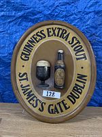Front view of an oval wooden bar sign plaque with raised Guinness bottle and glass and text around border.