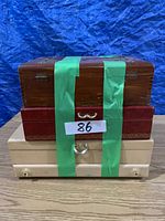 Photo of three stacked jewelry boxes: wooden top box with green tape, red middle box with gold trim, cream bottom box with metal knob