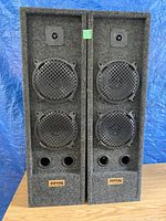 Pair of large Paragon standing speakers in gray carpeted enclosures with dual front ports and black speaker driver grilles.