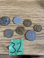 Photo showing seven assorted coins on a wooden surface with a green paper labeled '32'