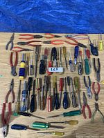 Overview of the assortment of pliers and screwdrivers laid out on a wooden surface with blue tarp background.
