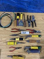 All hand tools laid out on a wooden surface, including wires, scrapers, screwdrivers, pliers, and shears