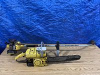 Full view of the McCulloch MAC 10-10 chain saw and the McCulloch MAC 80-SX weed wacker placed on a wooden surface in front of a blue background.