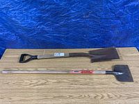 Photo showing two tools side by side: a metal shovel with D-handle and a steel ice chopper with wooden handle, placed on wooden surface with a blue backdrop