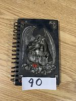 Front view of the notebook showing the metal dragon over the castle on the cover with red jewel accents.