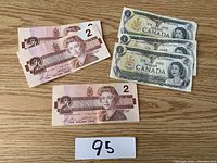 Photo showing three two-dollar Canadian bills, two of which have consecutive serial numbers, placed on a wooden surface next to a number card 95.