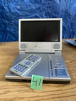 Front view of silver portable DVD player with screen open, built-in speakers, and remote control placed on top of the player.