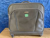 Exterior front view of the Samsonite garment suitcase showing outer fabric, front pocket, wheels, handle, and logo plaque.