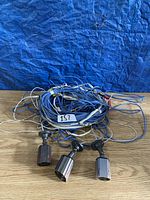 Three security cameras lying beside bundled blue and white cables on a wooden surface with a blue taped background, indicating cable length and quantity