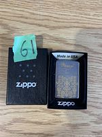 Zippo lighter with gold design displayed inside original black Zippo box that has white Zippo logo and 'Made in USA' sticker on top.
